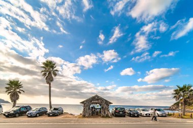 kyushu, japan - december 07 2021: Cars parked on the parking aera of Sakurai Futamigaura couple stones along Sunset beach overlooked by palm trees with a wooden hut made with tropical dried branches.