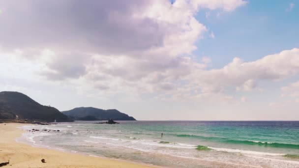 福岡県糸島海岸のターコイズブルーの海の波に乗ってパドルサーフィンをしている人が 櫻井二見ヶ浦の夫婦岩を背景に撮影 — ストック動画