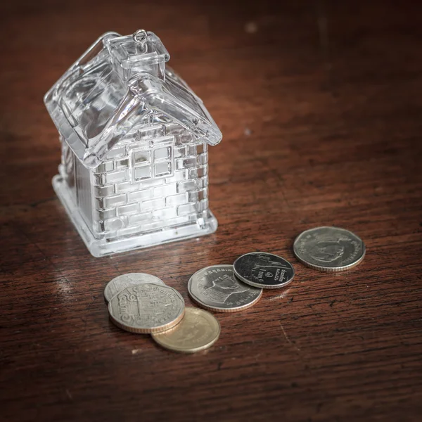 Klein huis en munten op hout achtergrondstructuur — Stockfoto