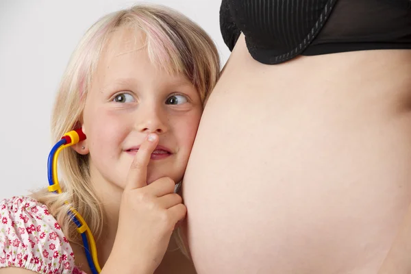 Маленькая девочка слушает живот беременной матери — стоковое фото