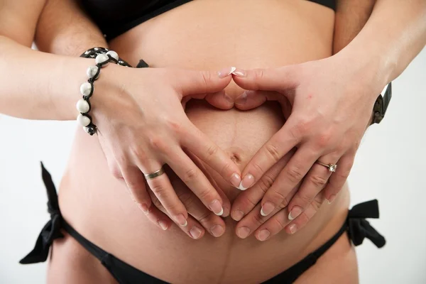 Zwangere buik met hart uit handen Stockfoto