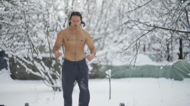 Atleta, un hombre con el pelo negro largo, en el invierno en la nieve, trenes en la calle — Vídeos de Stock