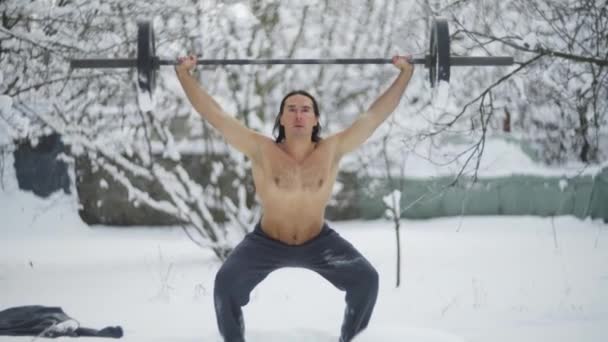 Athlete, black hair and a naked torso, trains in weightlifting, in the winter in the snow — стоковое видео