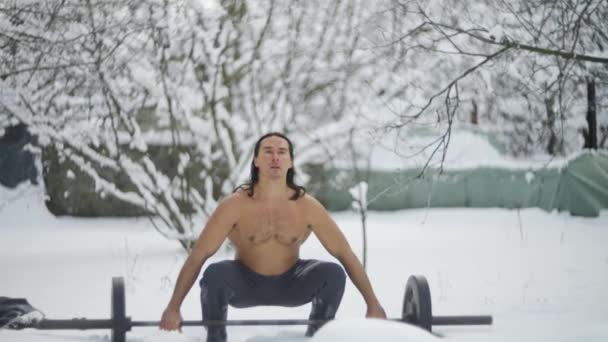 Muž je atlet, s dlouhými černými vlasy, v zimě ve sněhu, zvedne činku, zpomalený pohyb — Stock video