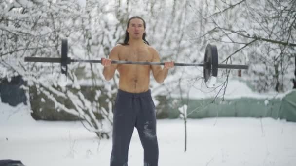 De man is een atleet, met lang zwart haar en een naakte romp, traint in gewichtheffen — Stockvideo