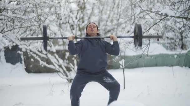 Man is an sportsman, weightlifting, in the winter in the snow, raises a barbell, trains — стоковое видео