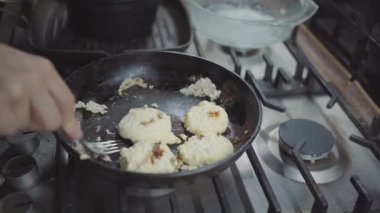 a woman in the kitchen, her pancakes are burnt, she rips a pancake from a frying pan