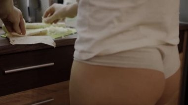 Külot giymiş seksi bir kız, mutfakta yemek hazırlıyor, peyniri ekmeğe sarıyordu.