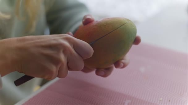 Женщина чистит, режет и ест манго — стоковое видео