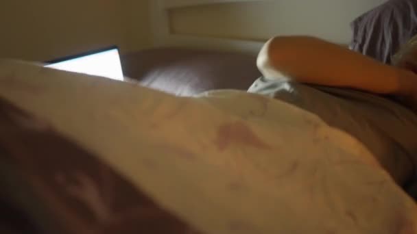 Девочка спит на кровати рядом с включенным ноутбуком, устав после работы — стоковое видео