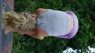 Blonde woman, trains on the street in the evening, doing stretching, slow motion, vertical view. High quality 4k footage.