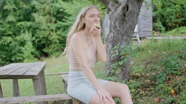女人是游客 坐在苹果树下的长椅上 在山里吃着新鲜的青苹果 一个女孩休息着 慢动作射击 高质量的4K镜头 — 图库视频影像