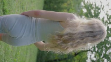 İnce, sarışın bir kadın bahçede çimlerin üzerinde duruyor ve yoga yapıyor. Ağır çekim. dikey görünüm