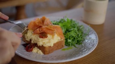 Kafedeki bir kadın çırpılmış yumurta, ekmek ve somon yer. Yakın çekim, yavaş çekim. Yüksek kalite 4k görüntü