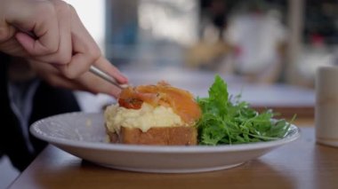 Kafedeki bir kadın çırpılmış yumurta, ekmek ve somon yer. Yakın çekim, yavaş çekim. Yüksek kalite 4k görüntü