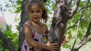 Küçük, güzel bir kız, elbise giymiş, ağaçta oturuyor, konuşuyor, gülümsüyor, gülüyor. Yardım çağırıyorum. Ağır çekim. Yüksek kalite 4k görüntü