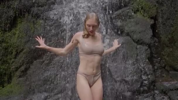 金髪の女の子がぬれた水着で滝から出てくる 女性の足を閉じるまで スローモーションに移動します 高品質4K映像 — ストック動画