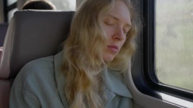 Yorgun bir kadın, Ukraynalı bir mülteci, trende dinleniyor. Genç sarışın. Yüzünü yaklaştır. Ağır çekim. Yüksek kalite 4k görüntü