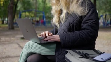 Bilişimci bir kadın sonbaharda parktaki bir bankta dizüstü bilgisayarda çalışıyor. Yüksek kalite 4k görüntü