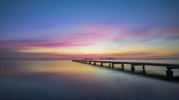 Mar Menor, Cartagena, İspanya 'da gün doğumunda güzel bir manzara. Göz kamaştırıcı, renkli bir gökyüzü ve denizin sakin sularına yansıyan. Ayrıca suda ahşap bir iskele görüyoruz. Huzur ve sükuneti iletir..
