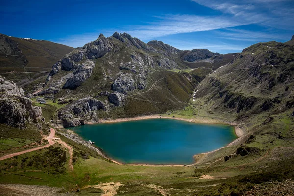 Panoramic view of the colorful Lago de la Cueva in the Parque Natural de Somiedo, in Asturias, Spain, with the snow-capped mountains in the background and green meadows. Ideal place for hiking and enjoying nature.