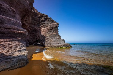 Plaj kristal ve şeffaf mavi ve yeşilimsi renklerle altın kum, gri ve mor kayalarla dolu. Yaz ve tatil hissi. Cartagena, Murcia Bölgesi, İspanya