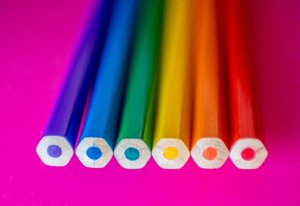 Six colored pencils seen from the top on pink cardboard that represent the colors of the rainbow and the flag of lgtbi rights