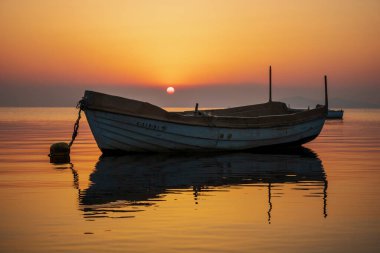 Murcia, İspanya 'daki Mar Menor' da gün doğumunun yatay fotoğrafı. Önünde bir balıkçı teknesi ve denizin sakin sularına yansıyan turuncu ve sarı bir gökyüzü var.