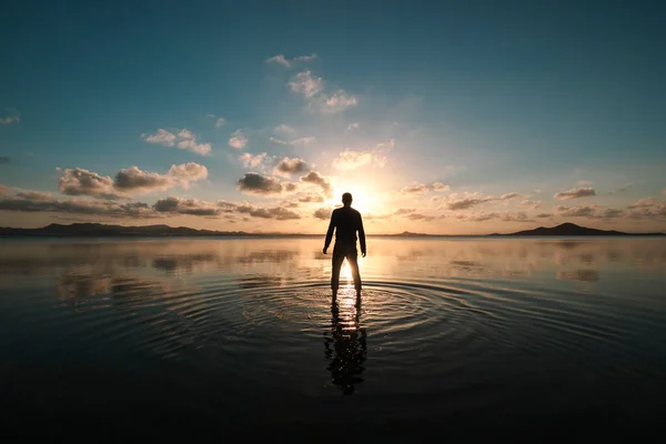 Silhouette of a man standing with his back facing at sunset over the shallow waters of the Mar Menor, Region of Murcia, Spain, creating ripples on the surface of the water