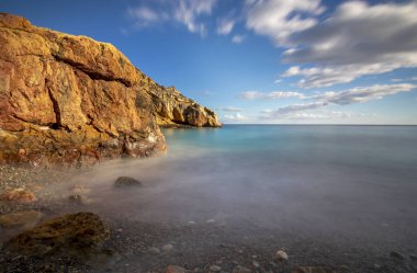 İspanya 'nın Cartagena sahilinde kayaların, denizin ve gökyüzünün renklerinin göze çarptığı küçük bir sahilin manzarası.