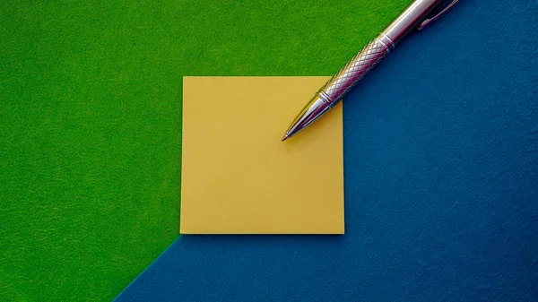 Horizontal composition in which a sticky note block appears with a silver pen on top and all this on a diagonal two-color background