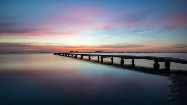 Beautiful wide landscape at sunrise in the Mar Menor, Cartagena, Spain. With a spectacular  very colorful sky and reflected in the calm waters of the sea. We also see a wooden jetty on the water. It transmits peace and tranquility.