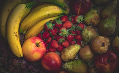 Still life of fruits on a kitchen table, banana, apple, nectarine, black grape, strawberries and pears, healthy and vegan food