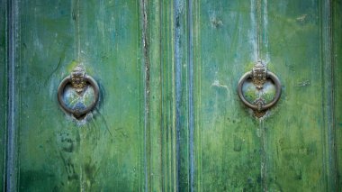 Old and worn double-leaf door with metal knockers or knockers and painted dark green