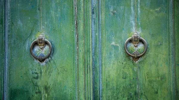 Old and worn double-leaf door with metal knockers or knockers and painted dark green