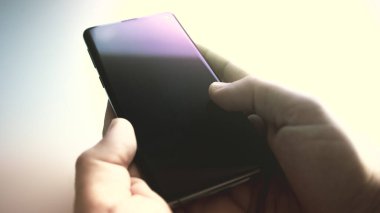 Siyah cep telefonu beyaz bir masaya kapatılmış ve yanında bir adamın elleri aranmayı bekliyor.