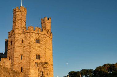 Caernarfon, UK- July 10, 2022: Warm glow of the suset light on  Eagle Tower of Caernarfon Castle in North Wales clipart