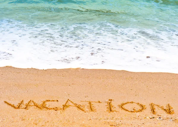 Διακοπές λέξη γραμμένο στην άμμο στην παραλία μπλε κυμάτων στο παρασκήνιο — Φωτογραφία Αρχείου