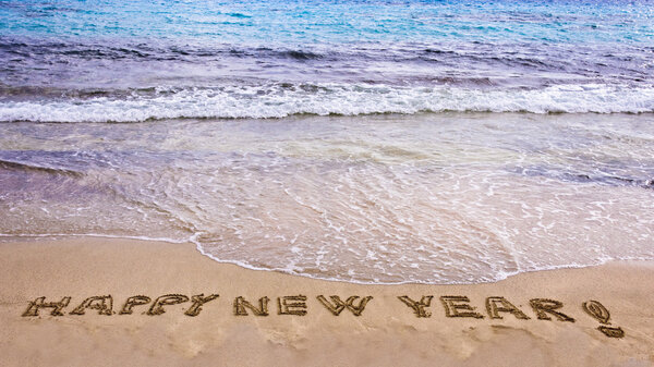 Happy new year and exclamation point written in the sand