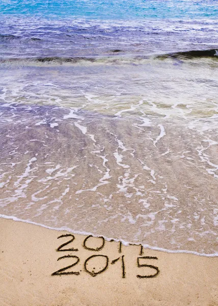 Año Nuevo 2015 viene concepto - inscripción 2014 y 2015 en una arena de playa, la ola está cubriendo 2014 — Foto de Stock