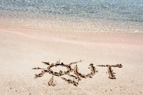 Mot "OUT" écrit sur du sable sur une belle plage, vagues bleues en arrière-plan — Photo