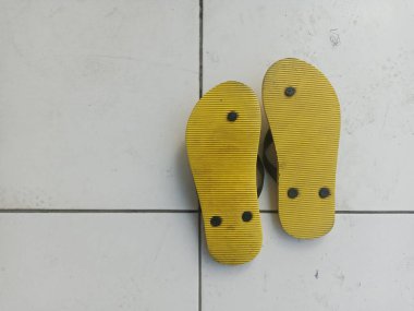 a pair of yellow flip-flops upside down on a white tiled floor