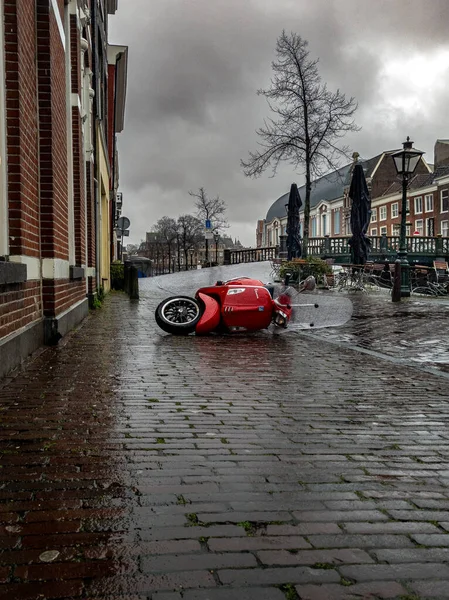 6 Şubat 2022, Leiden Hollanda, Kızıl Vespa şiddetli bir rüzgarla savruldu, yağmurun altında kaldırımda yatıyordu.
