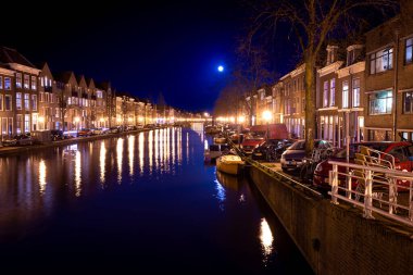 Leiden, Hollanda, 18 Mart 2022, tarihi evleri, küçük tekneleri ve dolunaylı kanalı gece görüşü.