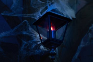 Örümcek ağındaki cadılar bayramı dekorunda kırmızı ışığı olan siyah fener.