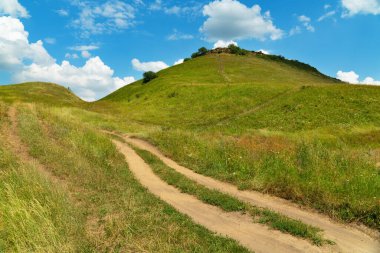 Yazın bulutlu bir gökyüzünün altında dağlardaki manzara toprak yolu.