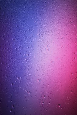 Renkli bir arka planda cam yüzeyine su damlaları düşer.