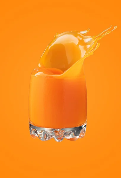 オレンジの背景に大きなスプラッシュのあるニンジンジュースのガラス — ストック写真