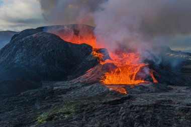 Reykjanes yarımadasında gündüz volkanik patlama. Kraterin açılışının yan görüntüsü lav akışıyla. İzlanda, GeoPark 'taki Fagradalsfall volkanı krateri. Bulutlar ve gökyüzündeki buhar