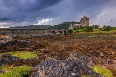 Skye Adası 'ndaki İskoçya' daki tarihi şato. Eilean Donan Şatosu alçak gelgitte bir adada. Kaleye yayalar için taş köprü. Ön planda yosun ve çimen olan taşlar.